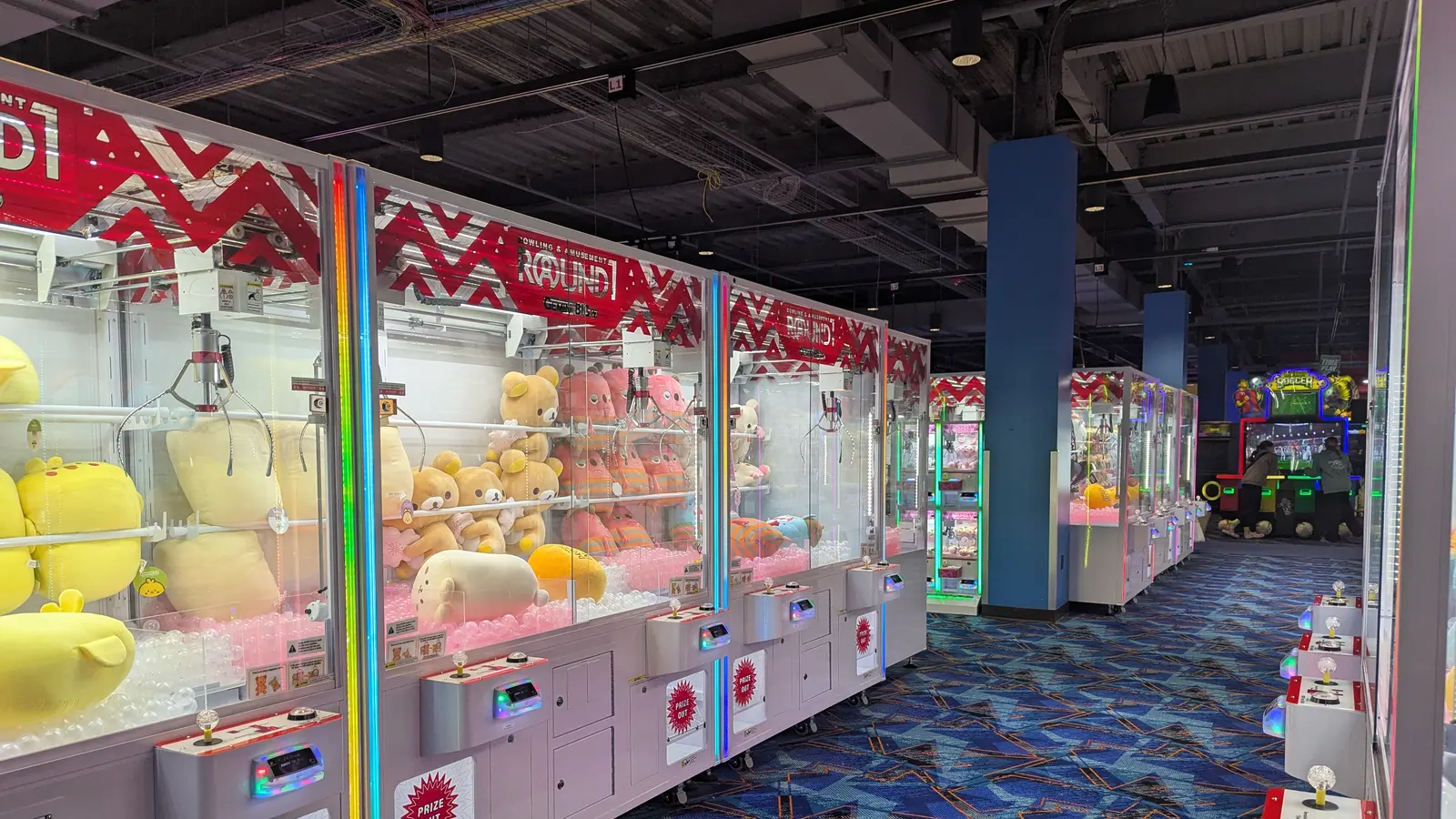 Pasillo de máquinas de garra (UFO catchers) con premios dentro de un centro de juegos
